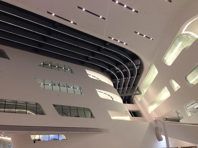 Moderne Innenarchitektur eines großen, hellen öffentlichen Raumes mit geschwungenen weißen Wänden, gestaffelter Beleuchtung und horizontalen Fenstern.