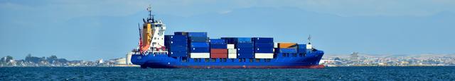 Container-Schiff, das über den Ozean segelt, mit einer Skyline und Bergen im Hintergrund
